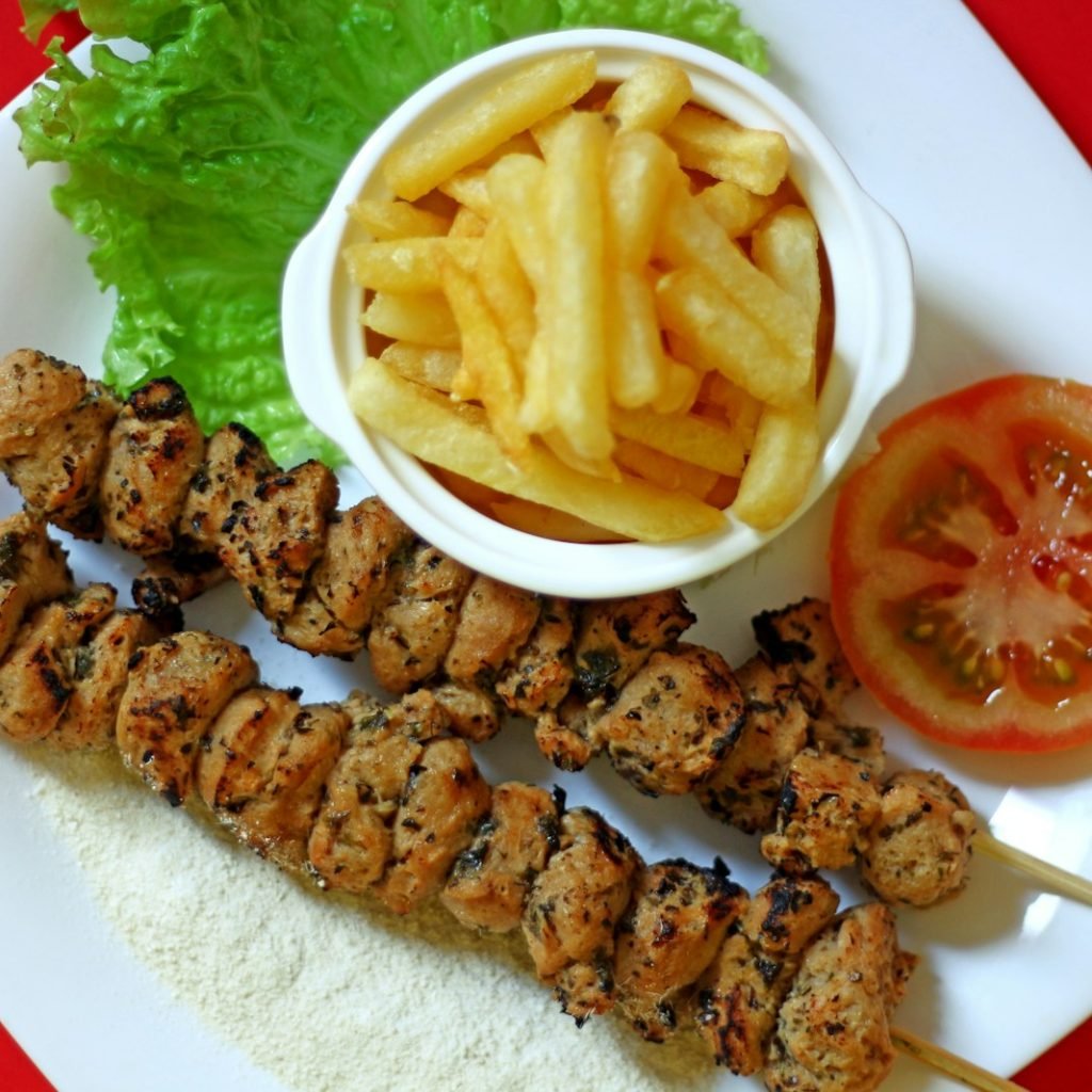A white plate topped with kebabs and french fries